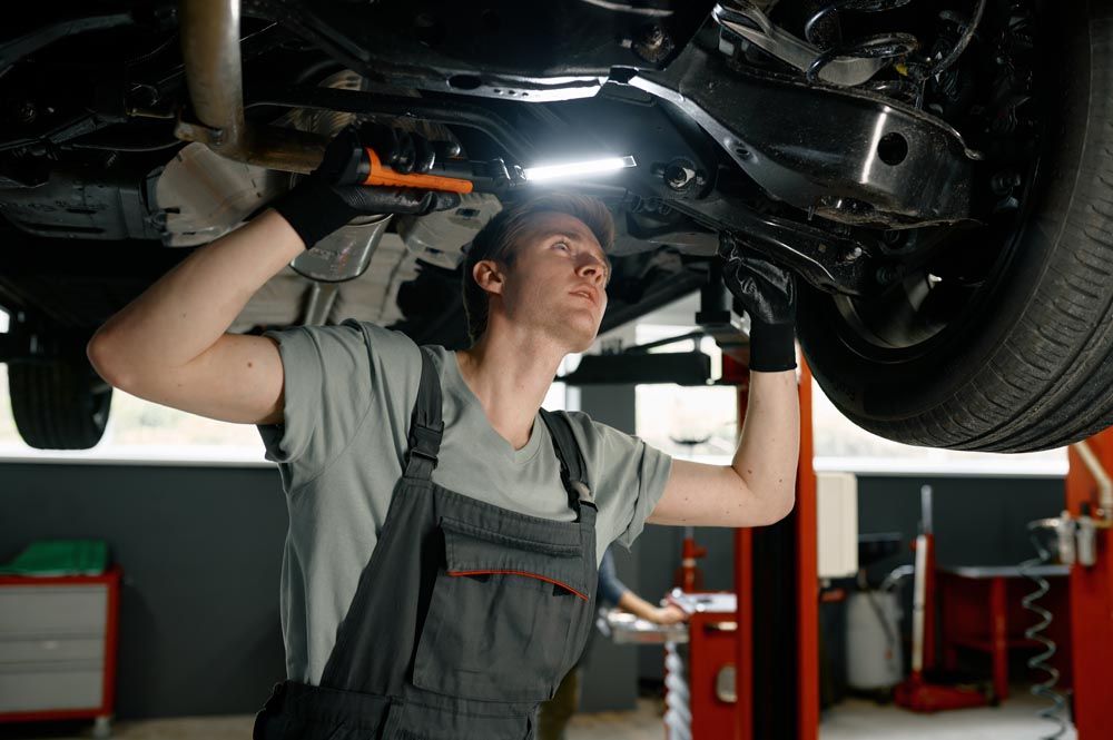 Male auto mechanic working under car lifted on elevator with flashlight.jpg